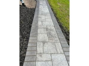Straight gray paver walkway installed beside a landscaped bed