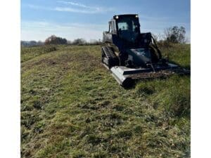 Skid steer grading a large open yard for landscaping work