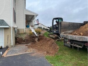 Excavation equipment preparing soil beside a residential driveway