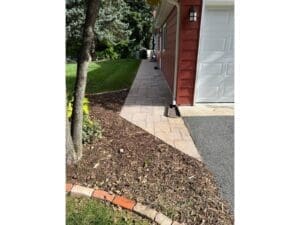 Concrete walkway and mulched landscape bed beside a garage