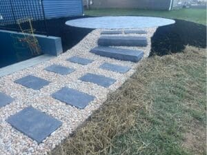 Curved stone walkway with gravel border leading to a backyard patio