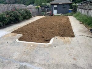 Freshly prepared landscape bed beside a concrete patio, previously a pool