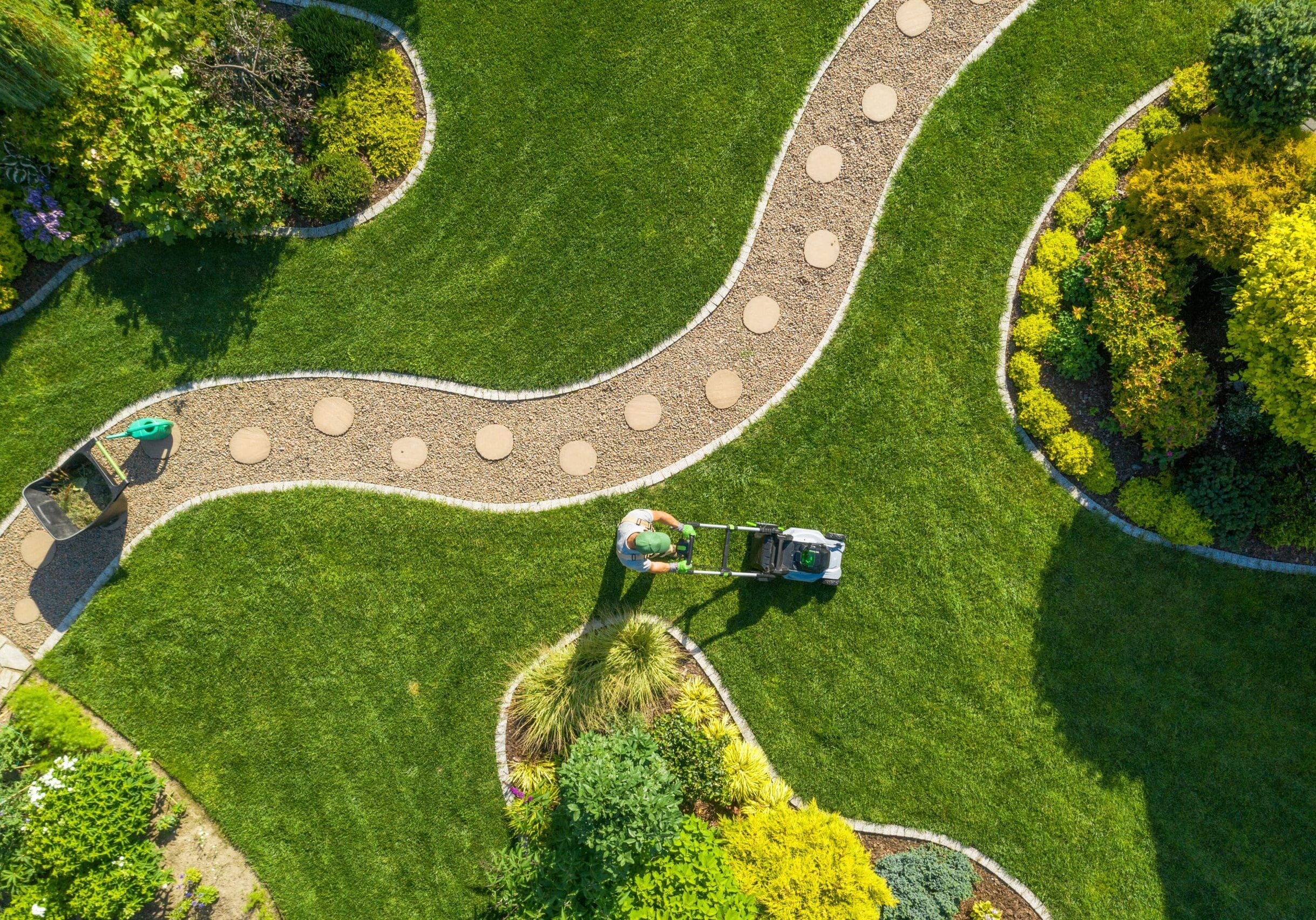 aerial view of a person moving a neatly landscaped lawn with stone walkways and garden beds